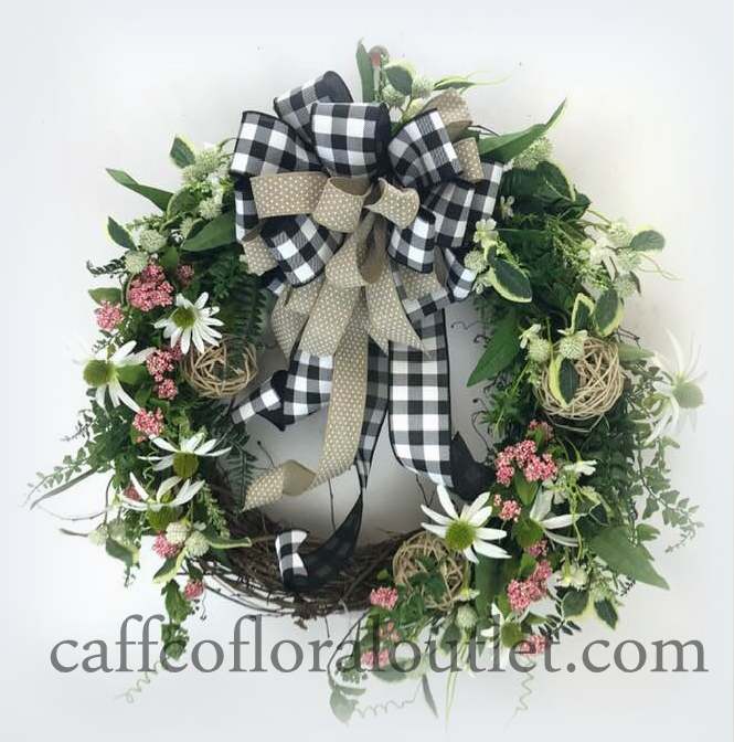 A grapevine wreath adorned with a black/white checked bow and faux daisies and delicate greenery