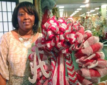 A smiling floral designer proudly displays a burgandy and white mesh ribbon wreath she has made
