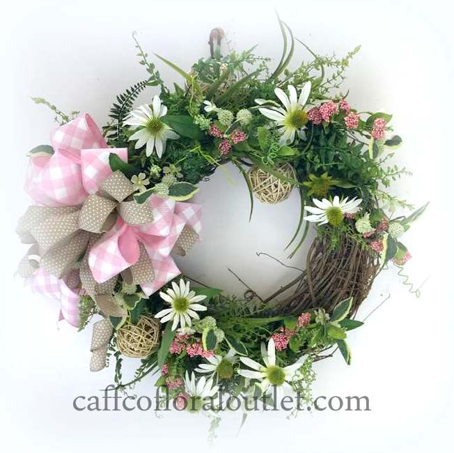 A grapevine wreath featuring delicate faux greenery, daisies, grapevine balls and a bow made from pink/white checked ribbon and neutral dotted ribbon